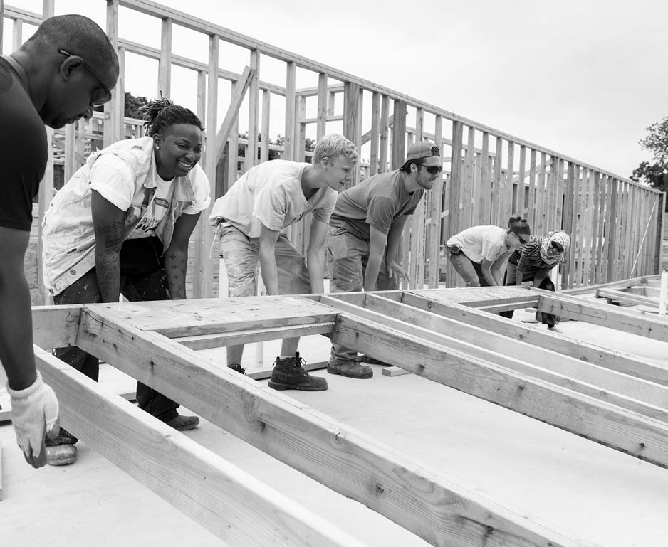 Volunteers lifting framed wall at construction site